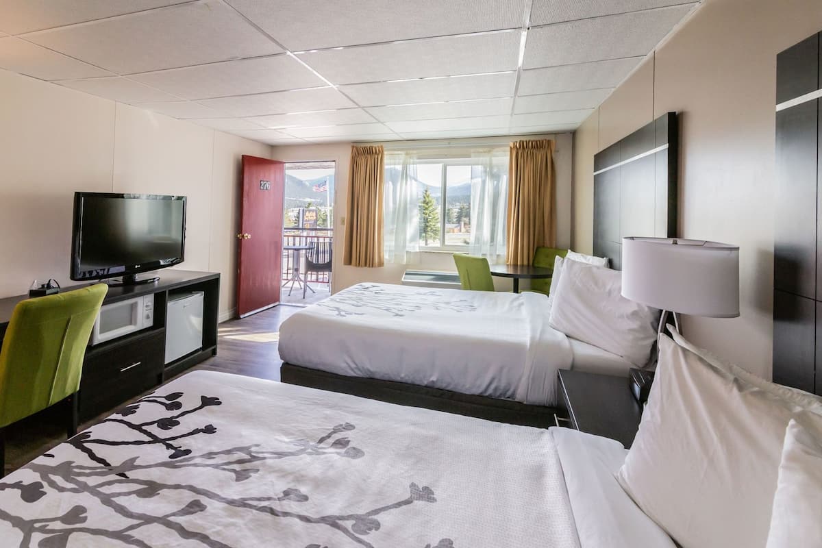 A hotel room with two beds, a television, a desk with a microwave, and a view of the outdoors.