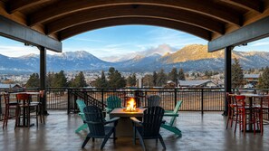 A covered outdoor seating area with a fire feature, chairs, and a view of mountains.
