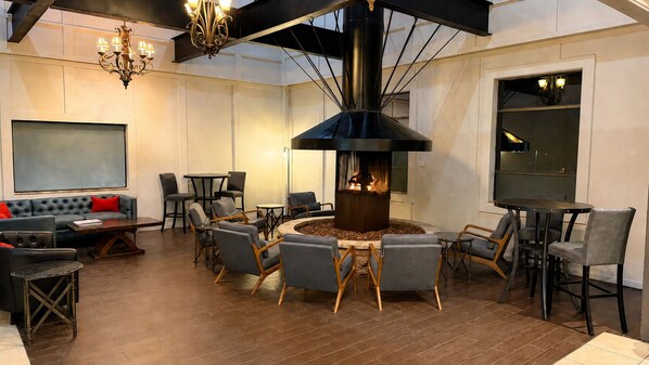A modern lounge with a central fire feature, seating arrangements, and a chandelier.