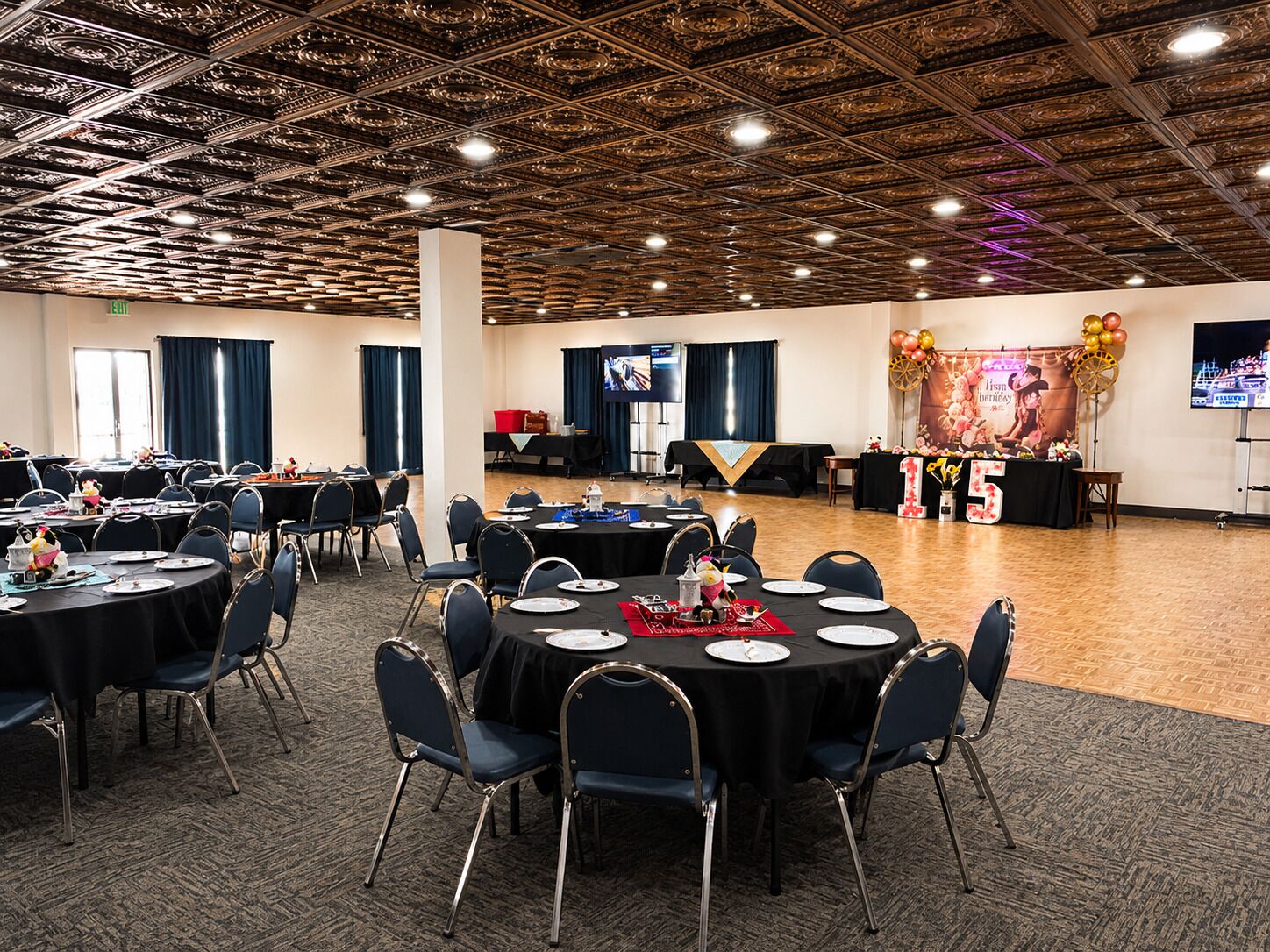 A banquet hall with round tables, chairs, and a stage with a banner.