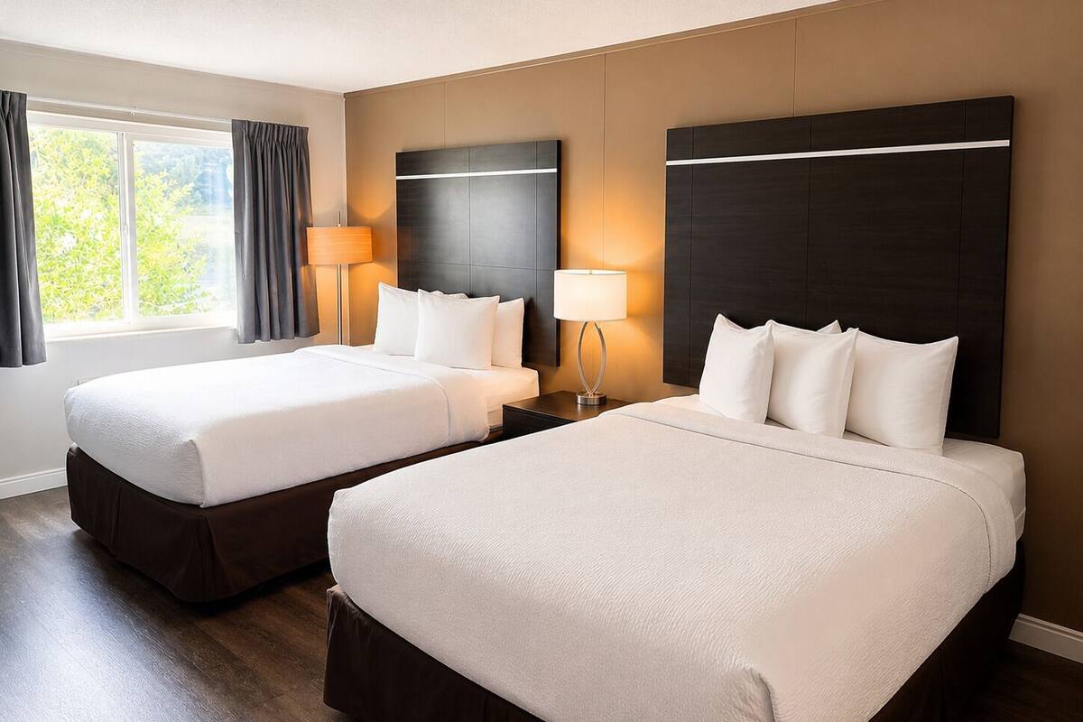 A hotel room with two beds, a large window with curtains, and a wall-mounted headboard.