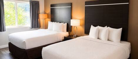 A hotel room with two beds, a large window with curtains, and a wall-mounted headboard.