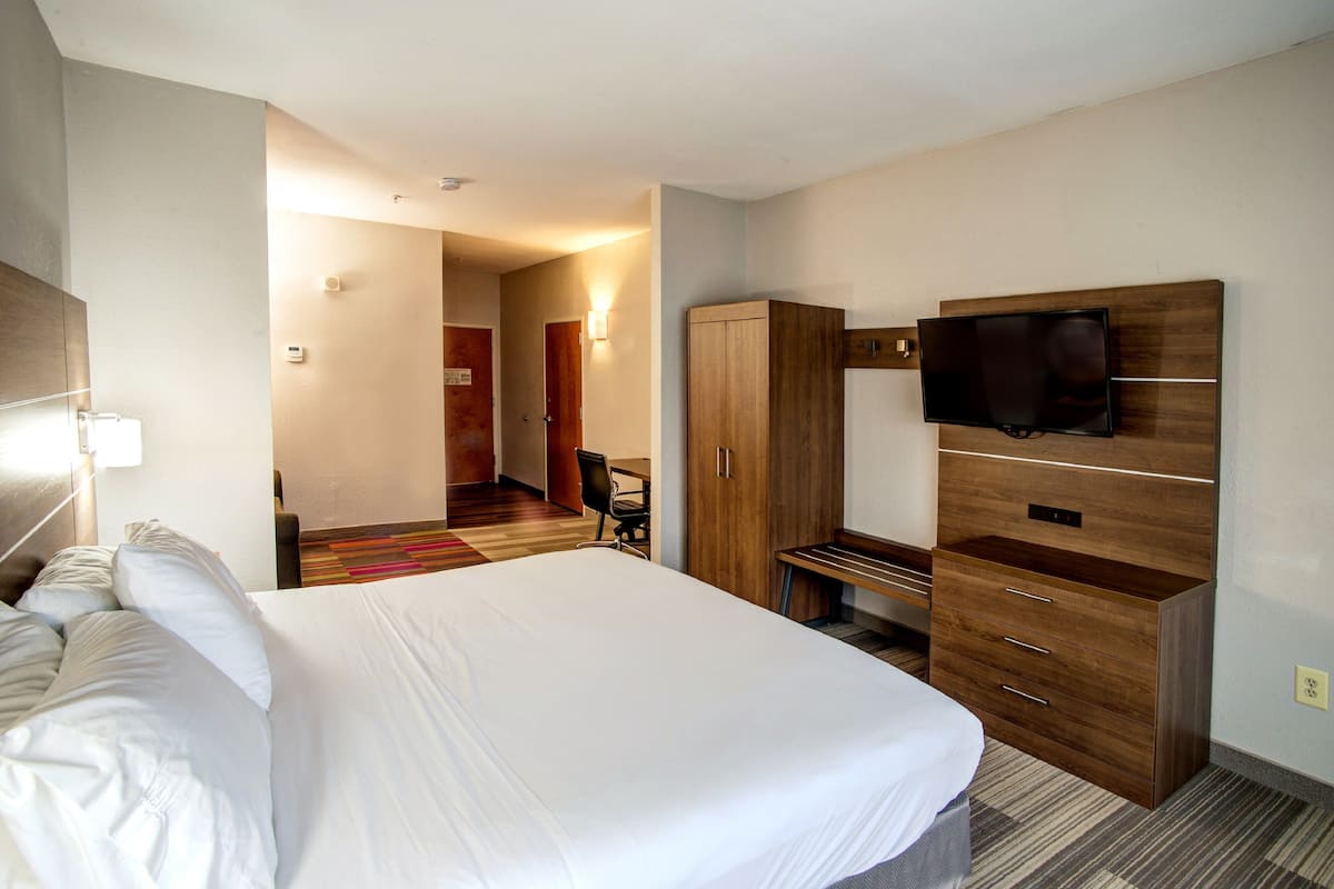 A hotel room with a large bed, a TV mounted on the wall, a wardrobe, and a desk.