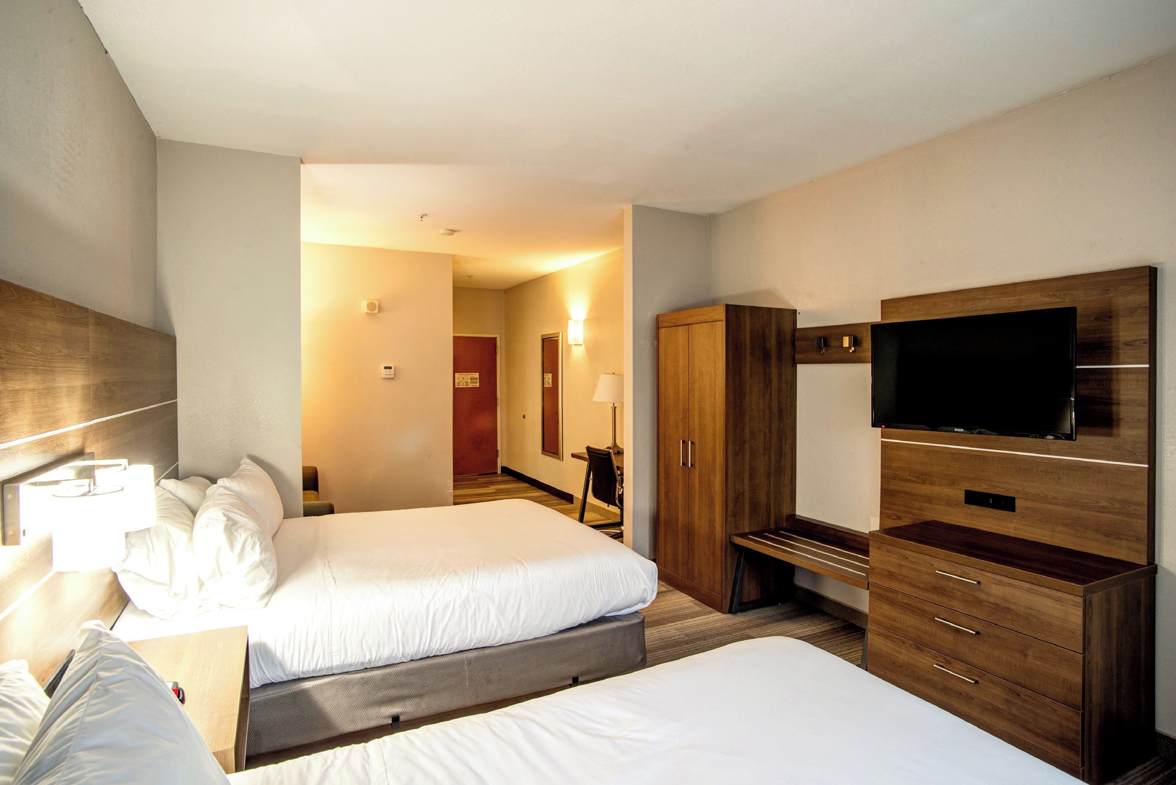 A hotel room with two beds, a TV, a wardrobe, and a desk with a lamp.