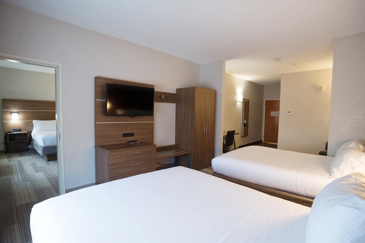 A hotel room with two beds, a TV mounted on the wall, a wooden wardrobe, and a desk.