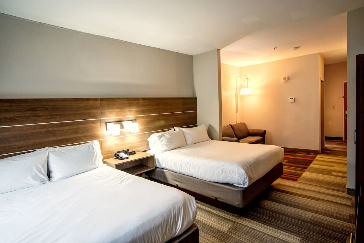 A hotel room with two beds, a wooden headboard, bedside lamps, a nightstand, and a carpeted floor.