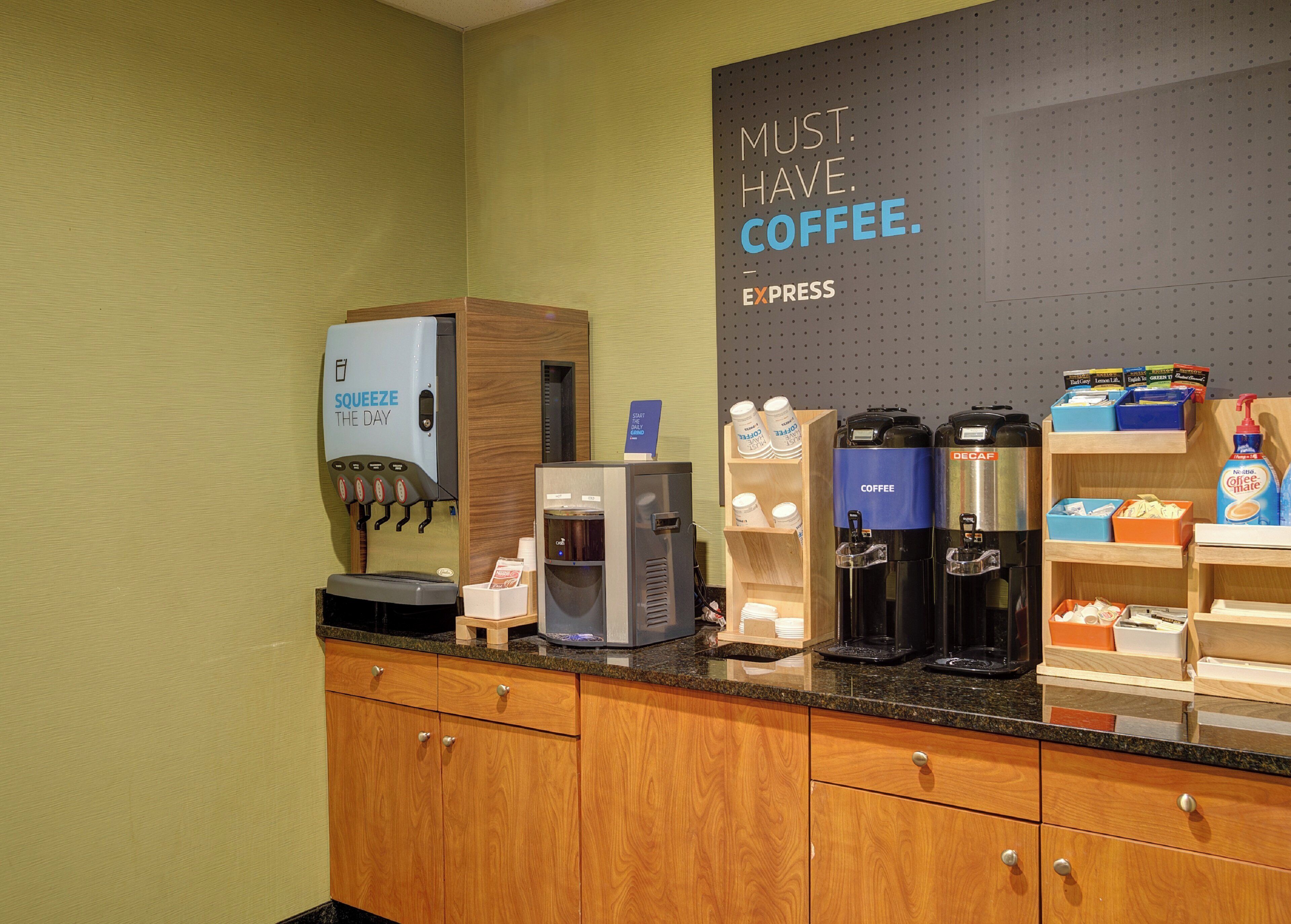 A coffee station with a dispenser, coffee makers, and a sign that reads 'MUST HAVE COFFEE.'