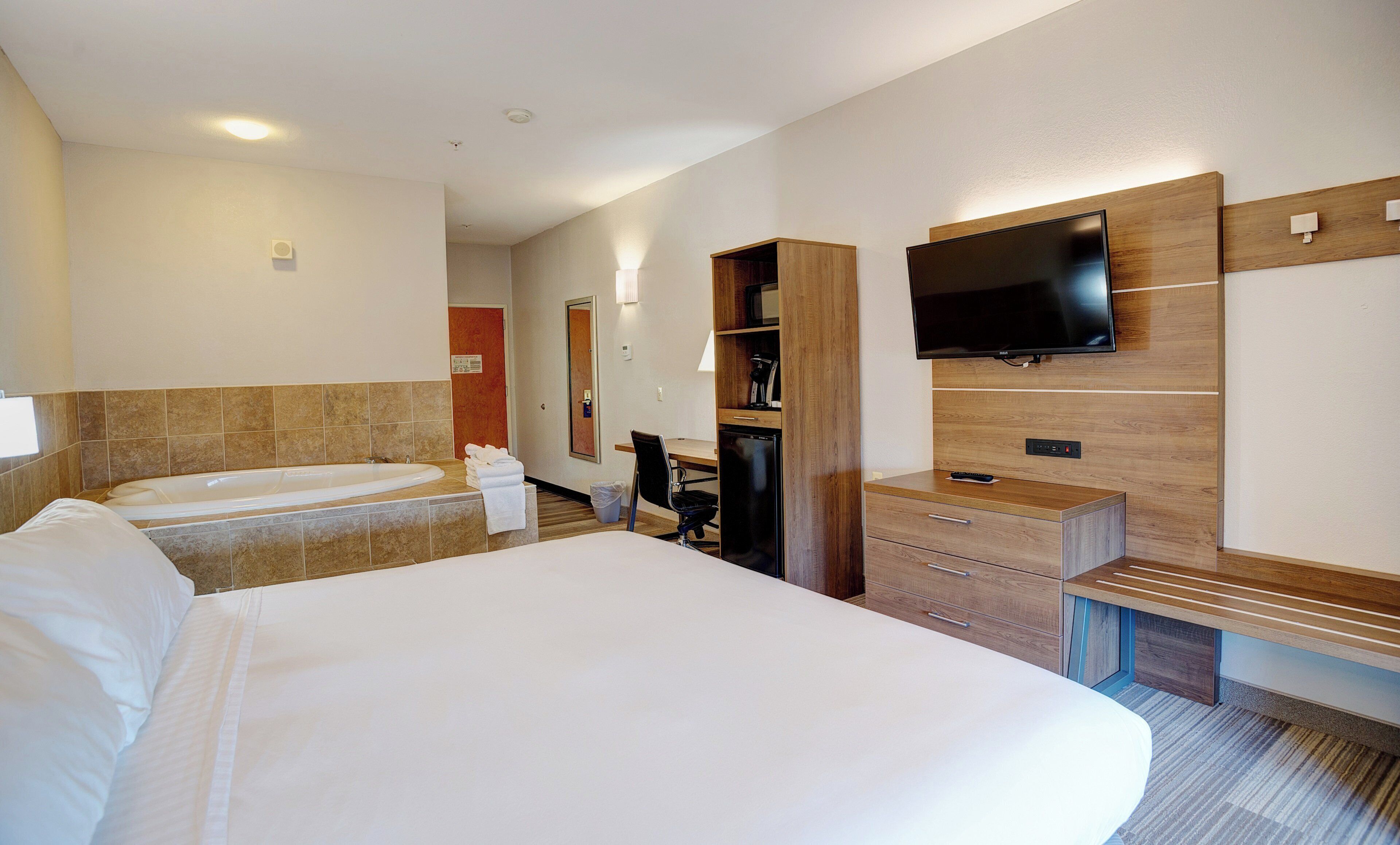 Une chambre d’hôtel avec un grand lit, une salle de bain séparée avec une baignoire, un bureau avec une chaise, un téléviseur fixé au mur et un petit réfrigérateur.