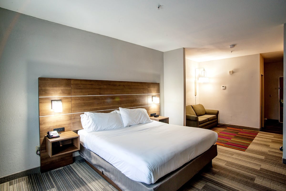 A hotel room with a large bed, a nightstand with a phone, a chair, and a carpeted floor.