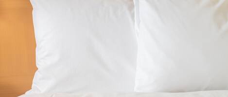 A bed with white bedding and pillows against a wooden headboard.