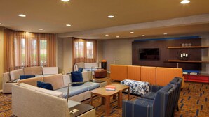Una habitación de hotel con un sofá, una mesita, un televisor y una estantería.