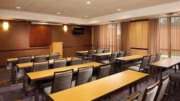 A conference room with multiple tables and chairs, a television on the wall, and large windows with curtains.