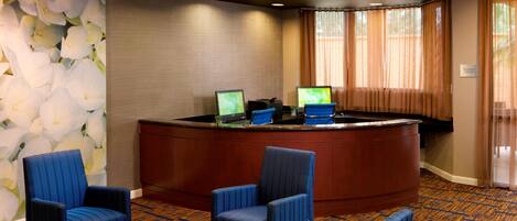 Zona de recepción con un mostrador curvo, dos monitores de computadora y varias sillas azules.