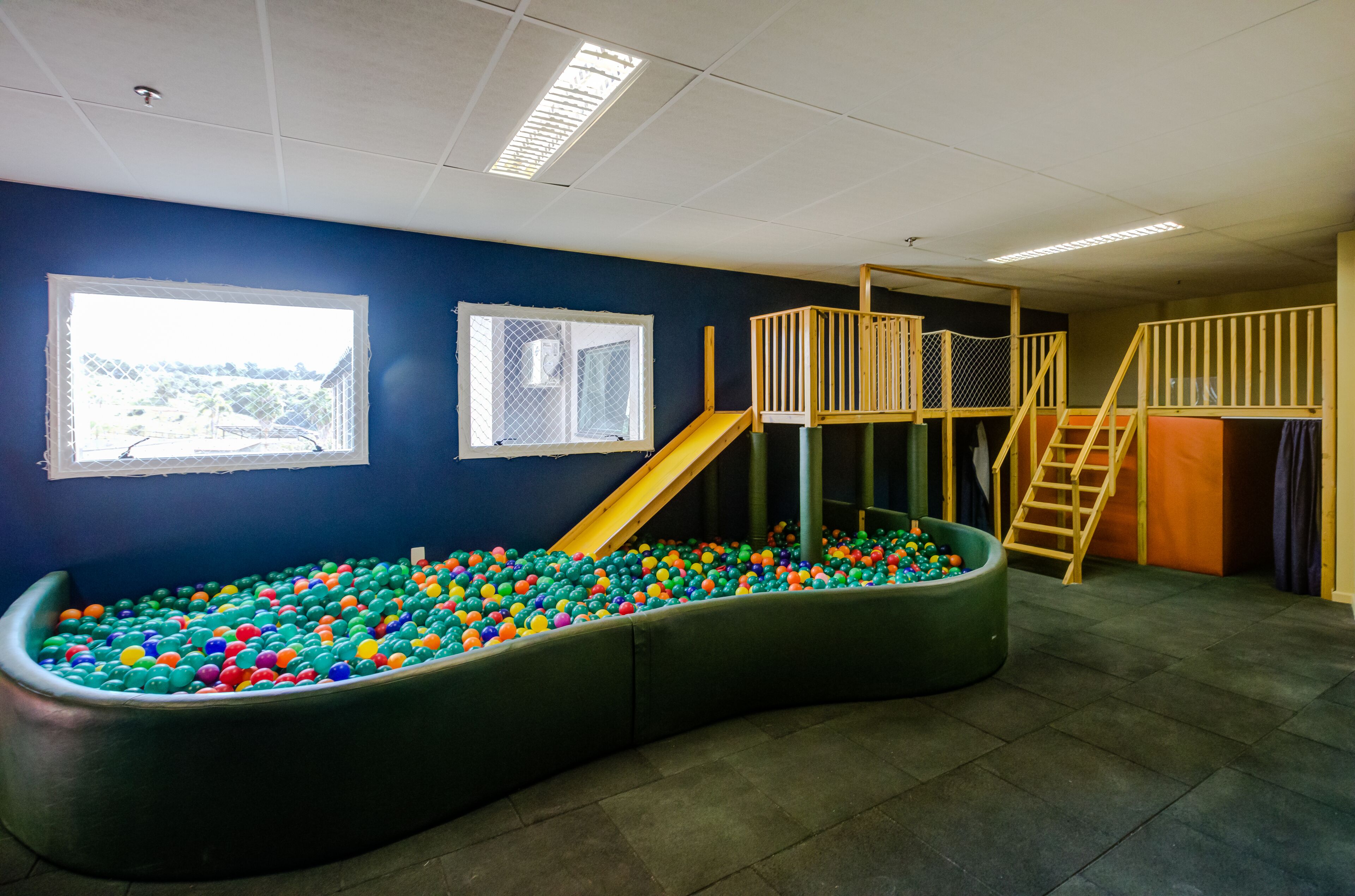 Uma área de recreação com piscina de bolinhas, escorregador e uma pequena estrutura de madeira para escalar.