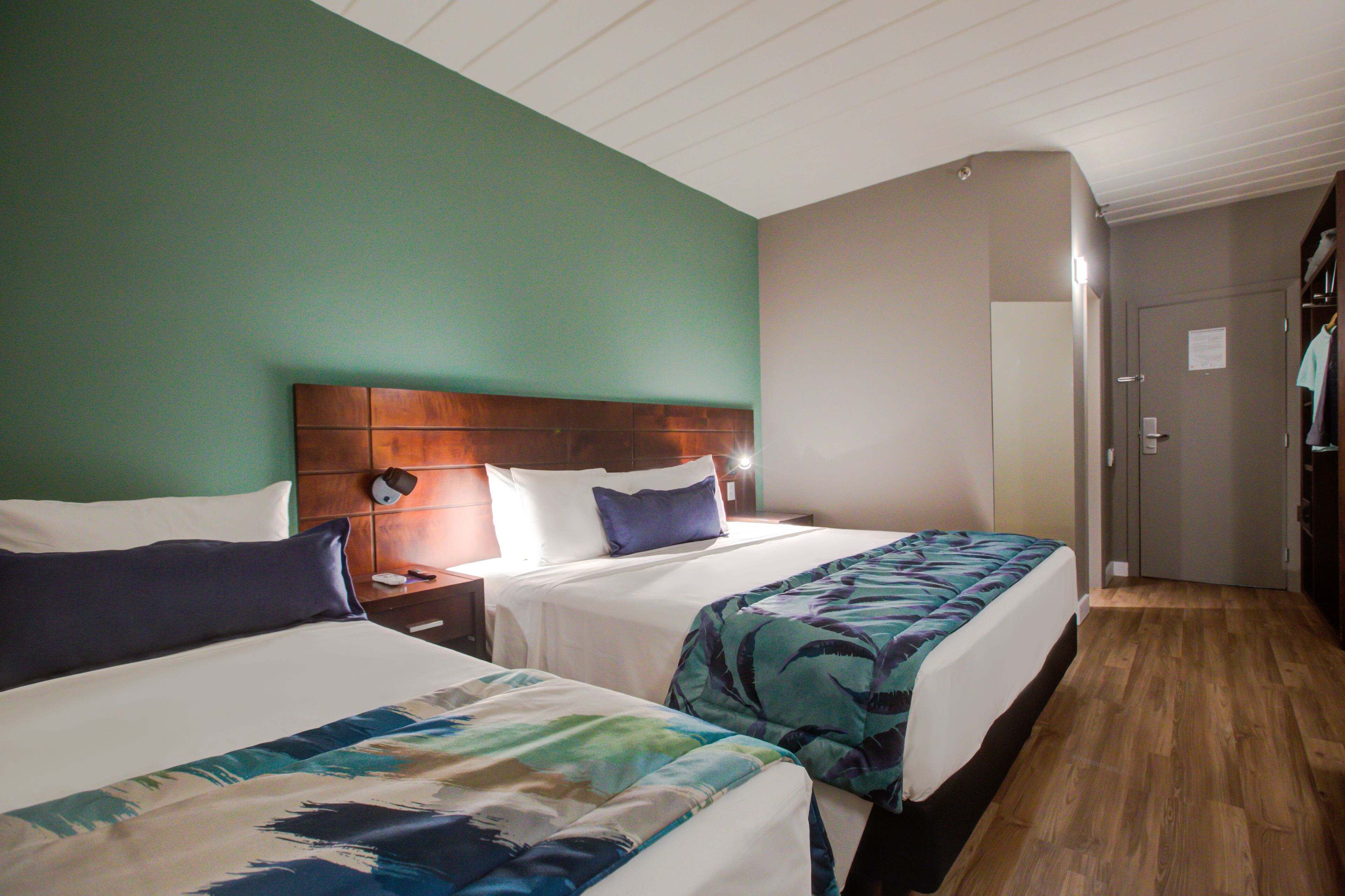 A hotel room with two beds, wooden headboards, and a green wall.