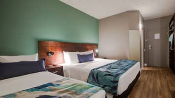 A hotel room with two beds, wooden headboards, and a green wall.