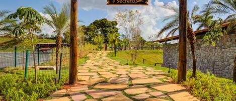A stone pathway leading to a wooden archway with a sign reading "Jardim Secreto".