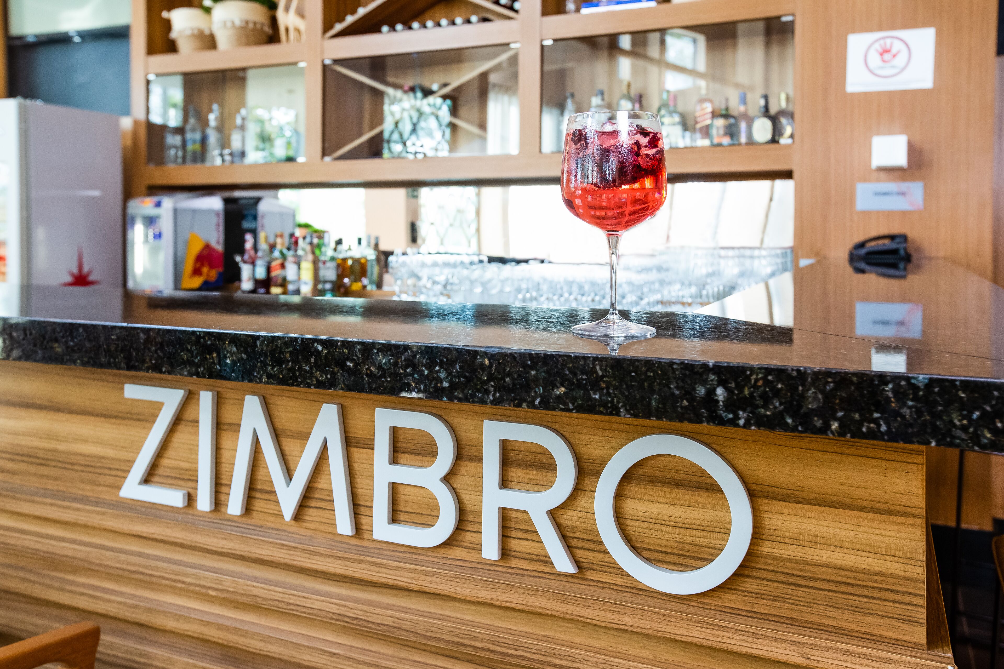 Una barra con una copa de vino tinto y el nombre "ZIMBRO" en el panel de madera.