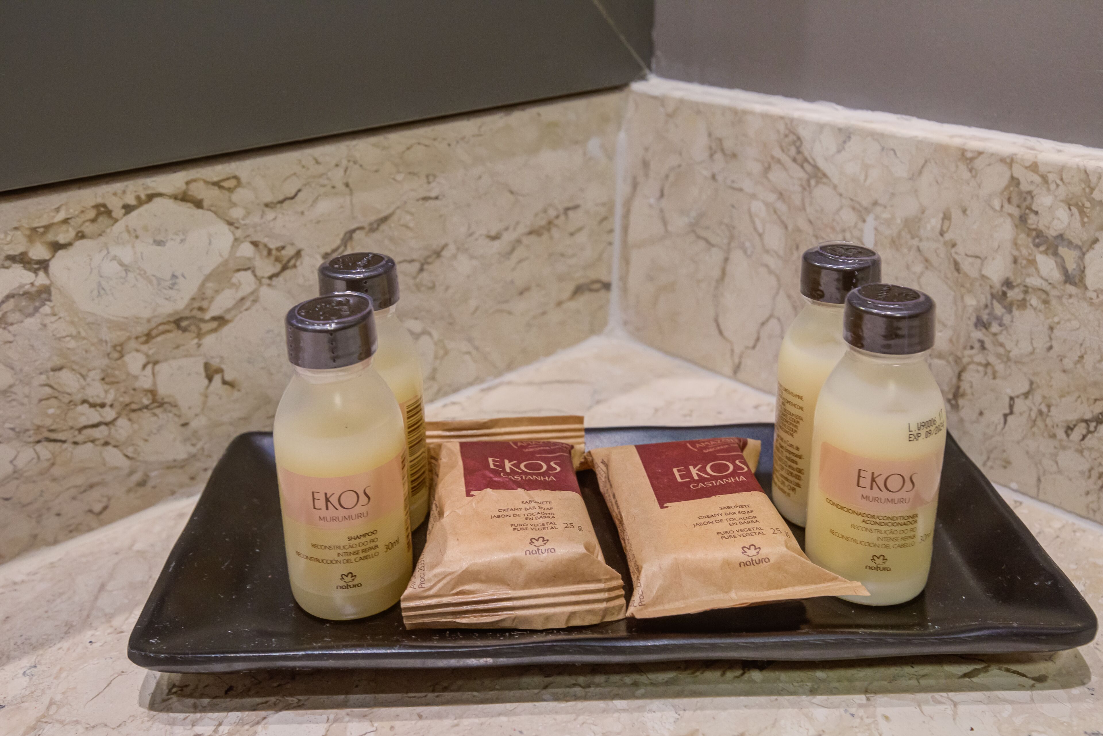 Een dienblad met drie flessen EKOS shampoo en conditioner, en drie kleine zakjes EKOS douchegel.