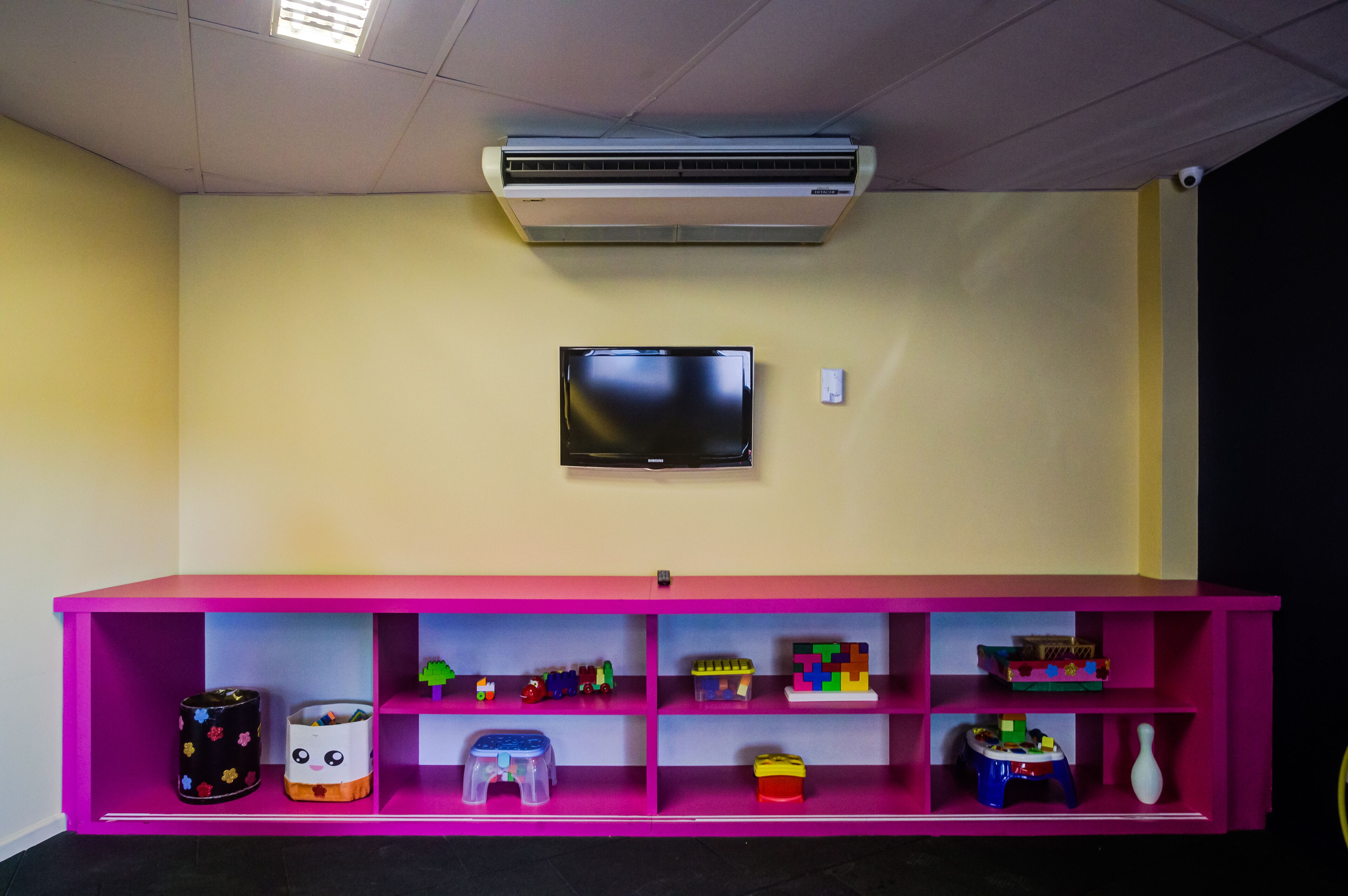 A room with a pink shelf unit containing toys and a flat-screen TV mounted on the wall.