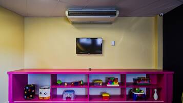 A room with a pink shelf unit containing toys and a flat-screen TV mounted on the wall.