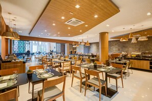 A modern dining area with wooden tables and chairs, a kitchen in the background, and pendant lighting. - Cyan Resort by Atlantica (Itupeva)