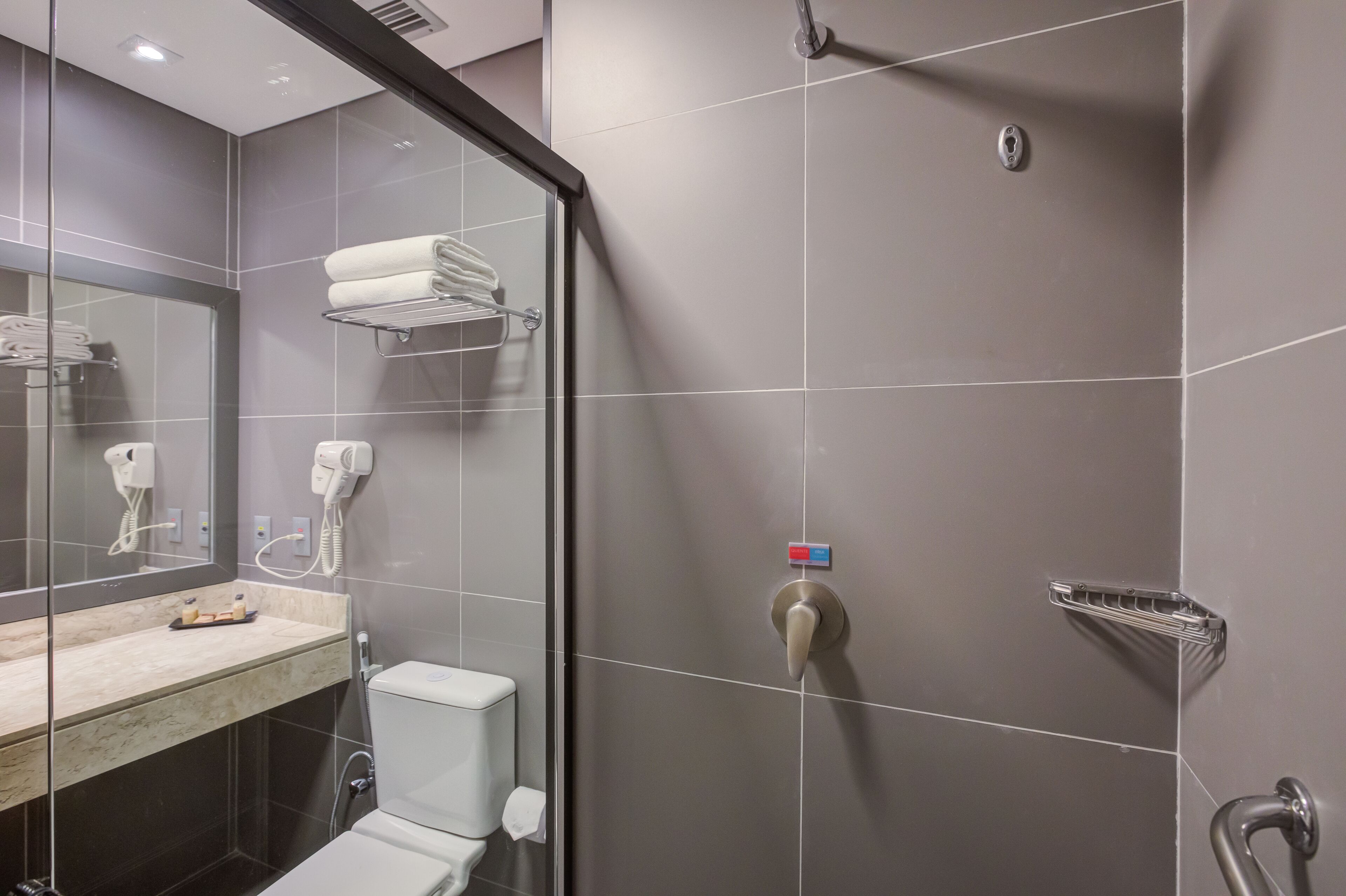 Un bany modern amb un espai de dutxa de vidre, un vàter, un lavabo amb taulell de marbre i un suport de tovalloles amb tovalloles doblegades.