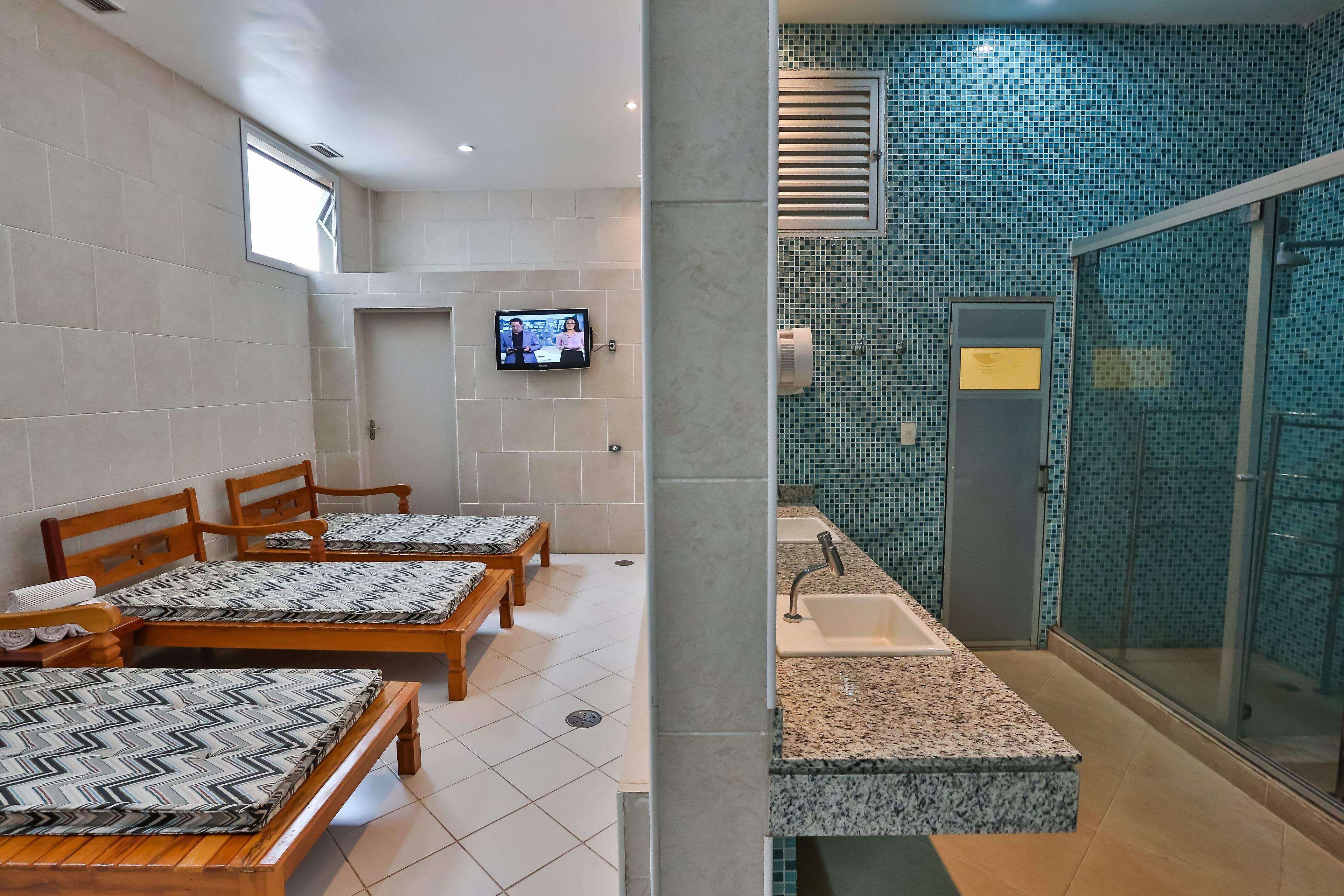 Habitación de hotel con cuatro camas de madera, un televisor montado en la pared, un lavabo con encimera de granito y zona de ducha con mosaicos azules.