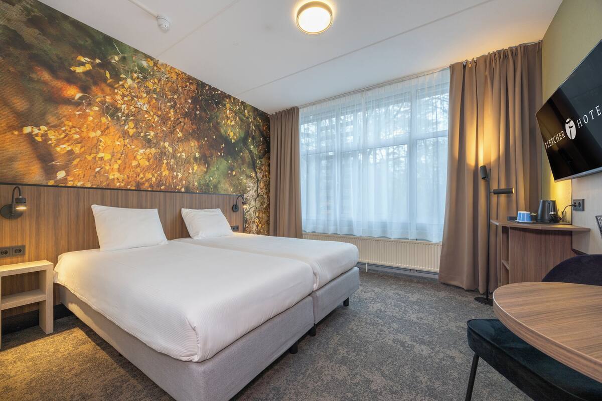 Une chambre d’hôtel avec un grand lit, une télévision, un bureau et une fenêtre avec des rideaux.