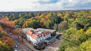 A large, white building with a red-tiled roof, surrounded by autumn-colored trees. - Fletcher Hotel-Restaurant Apeldoorn (Apeldoorn)