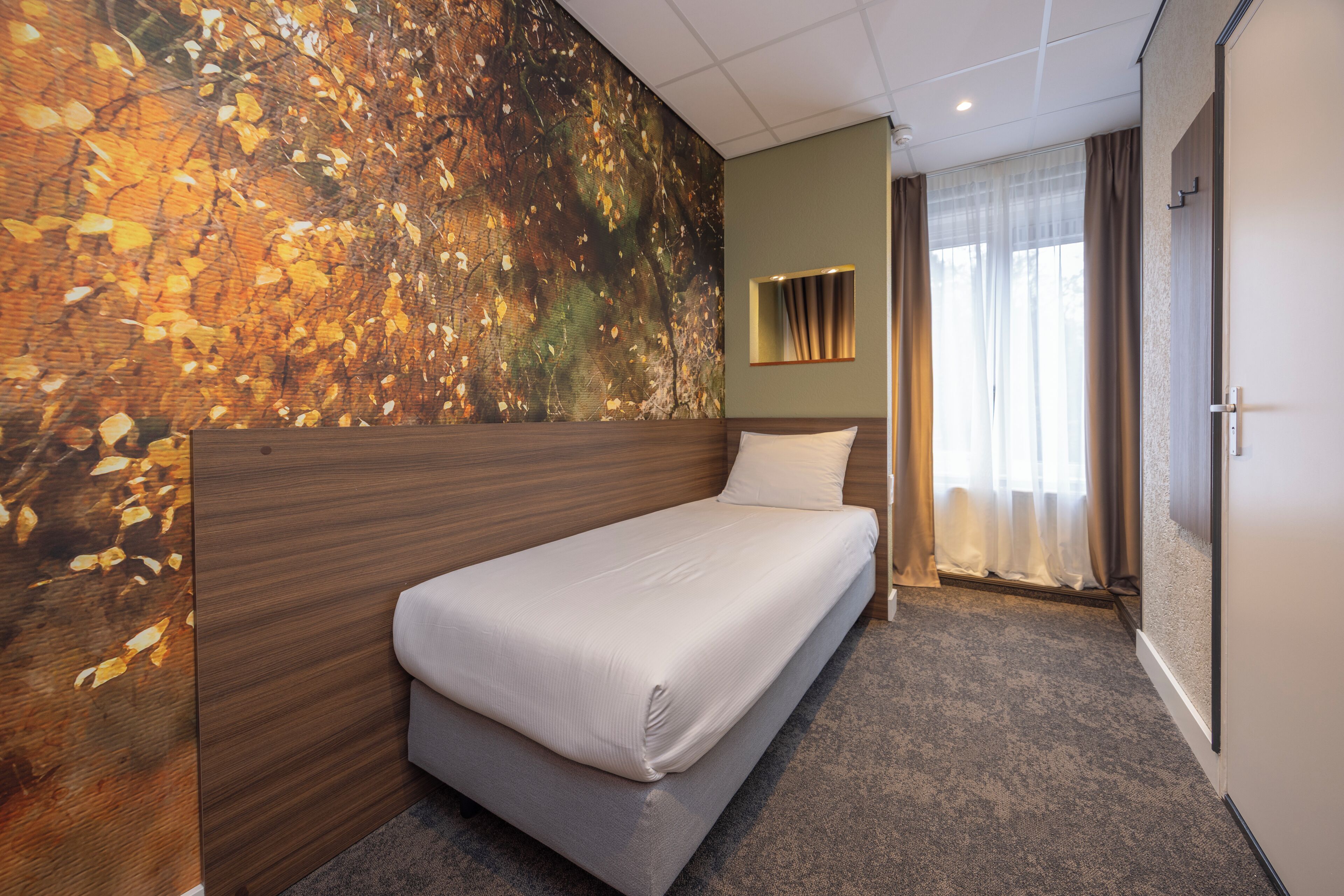 Une chambre d’hôtel avec un lit, une grande fresque murale, une fenêtre avec des rideaux et une porte.
