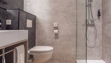 Un baño moderno con ducha de vidrio, inodoro blanco y tocador con espejo y toallero.
