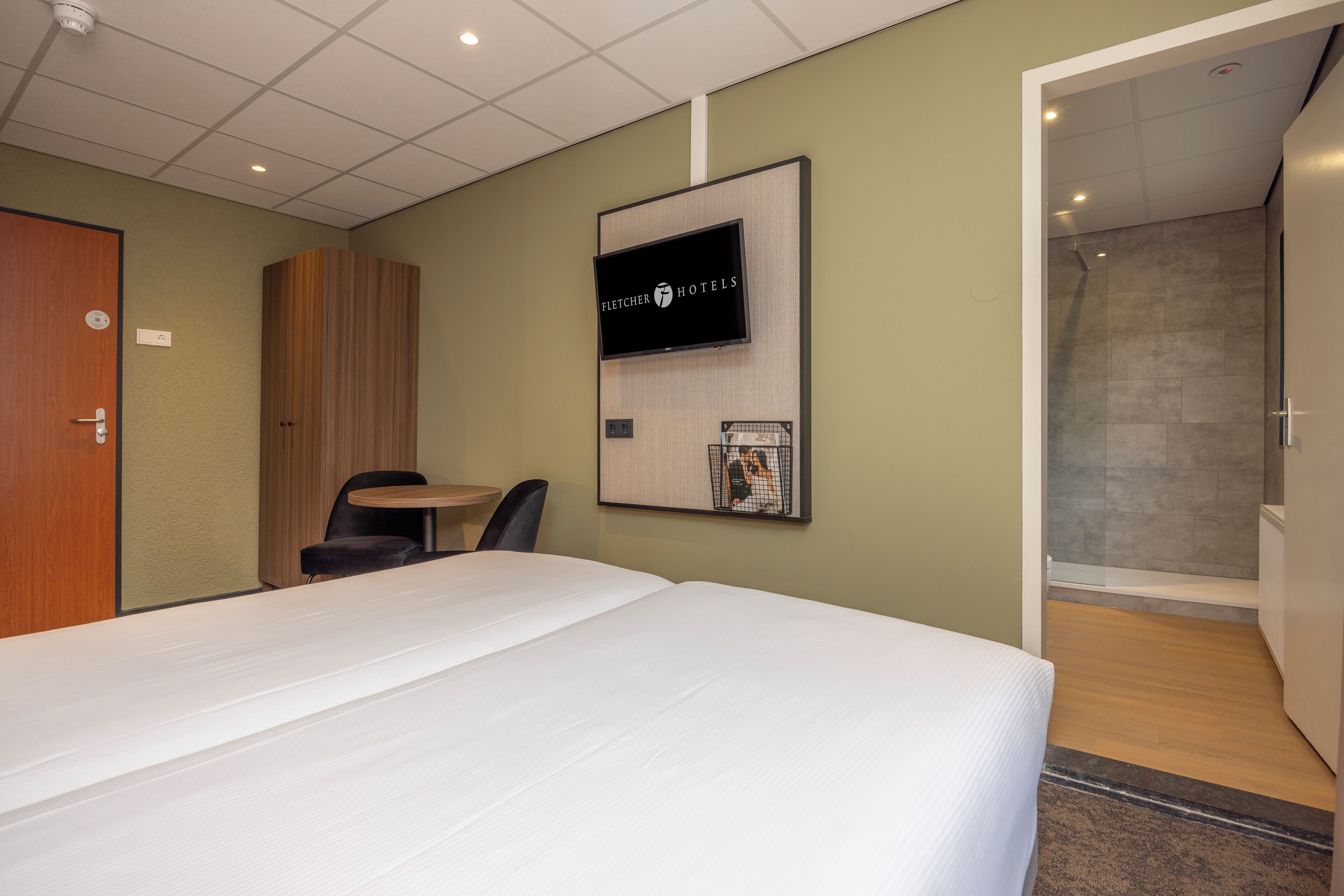 Une chambre d’hôtel comprenant un lit, un bureau, une chaise, un téléviseur fixé au mur et un espace douche.