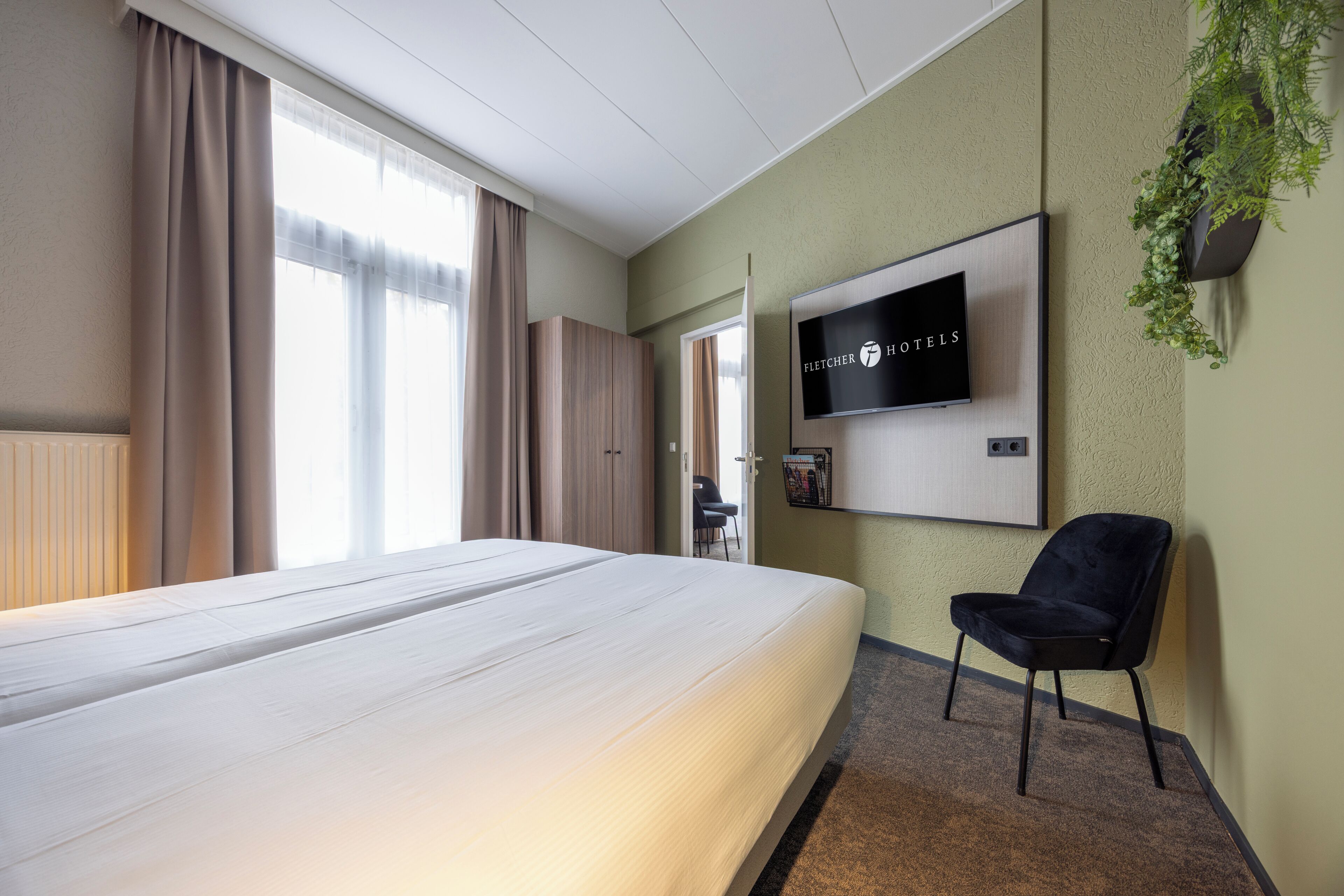 A hotel room with a bed, a TV mounted on the wall, a chair, and a potted plant.