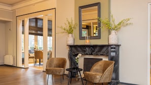 A room with a fireplace, two armchairs, a small table, and a mirror on the wall. - Fletcher Hotel-Restaurant Apeldoorn (Apeldoorn)