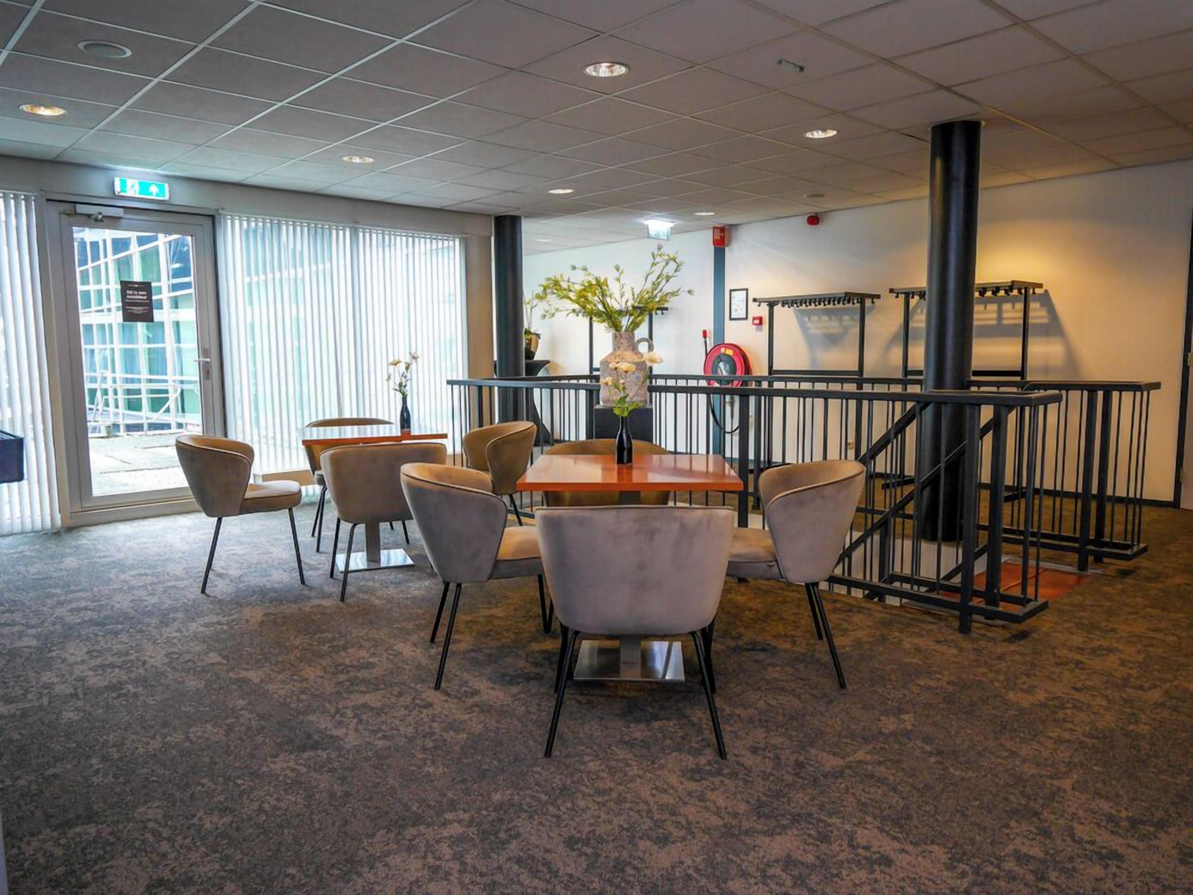 A conference room with a wooden table, six chairs, a vase with flowers, a clock, and a staircase with a railing.