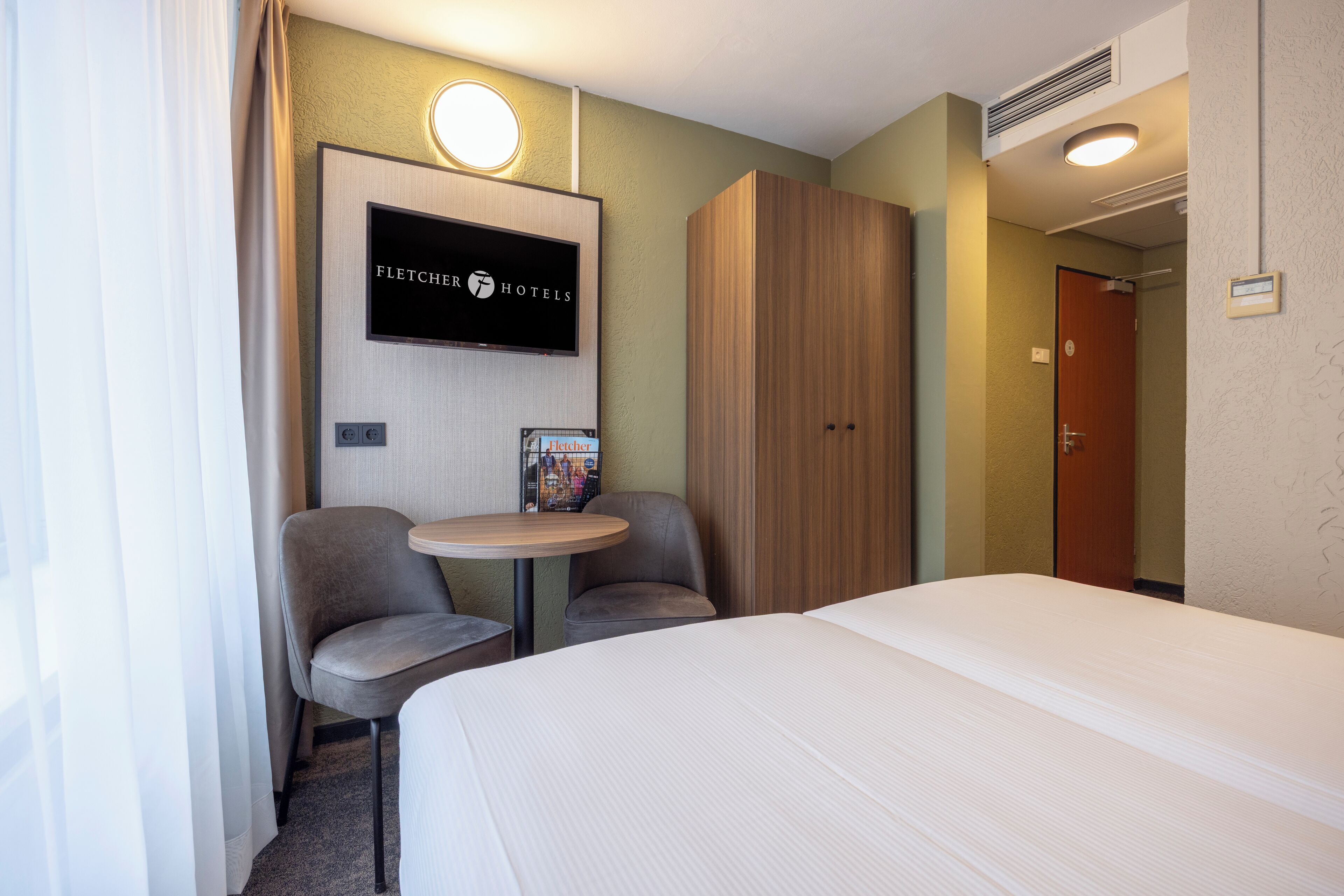 Habitación de hotel con cama, dos sillas, una mesita, televisor y armario.