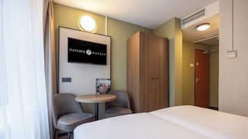 Ett hotellrum med en säng, två stolar, ett litet bord, en tv och en garderob.