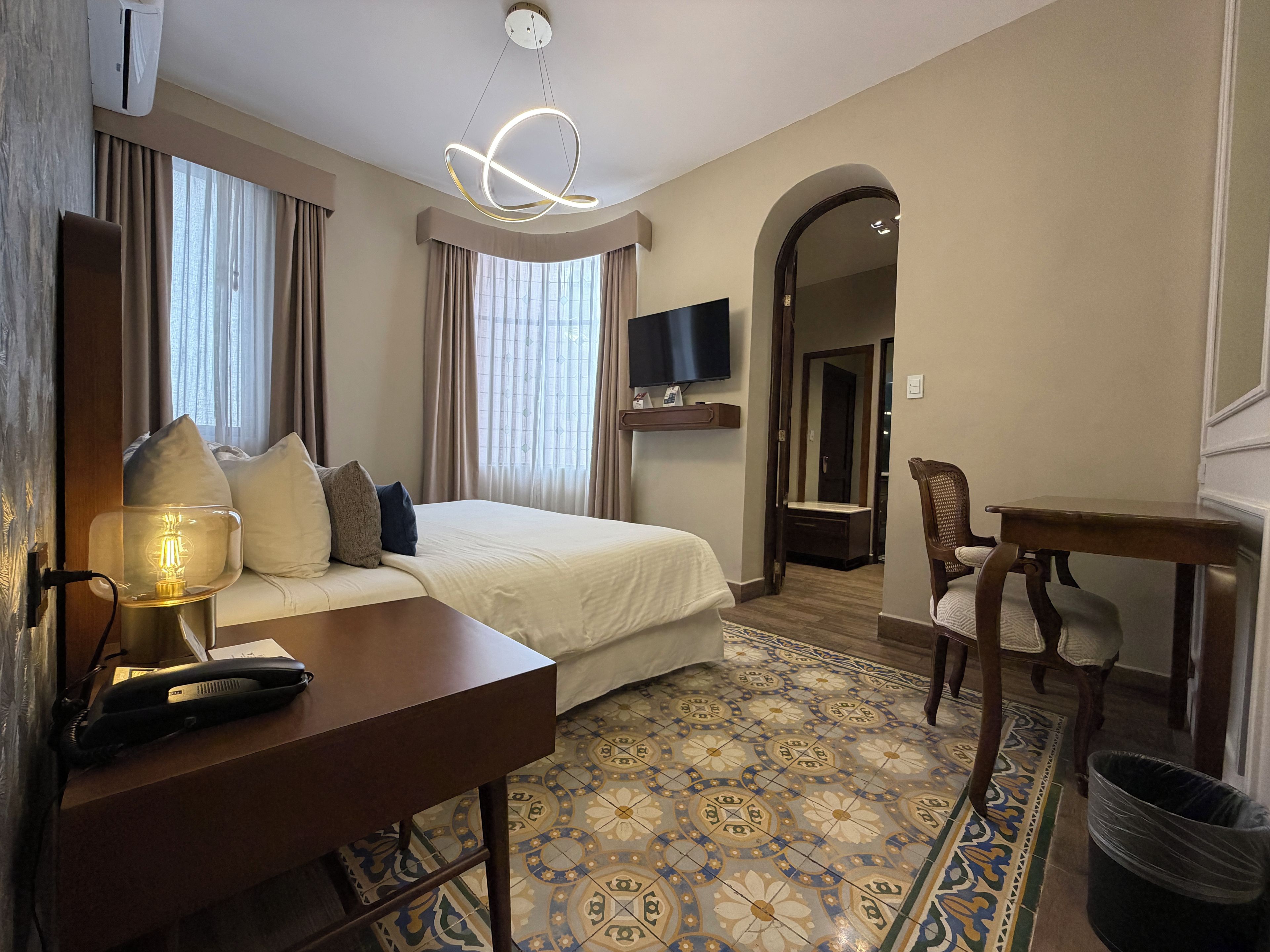 A hotel room with a bed, bedside table, lamp, TV, and a chair.