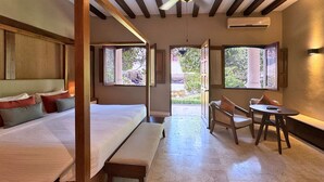 A bedroom with a bed, bench, and a table with chairs. There are windows providing natural light and views of the outdoors. - Casa Lucia Hotel Boutique (Mérida)