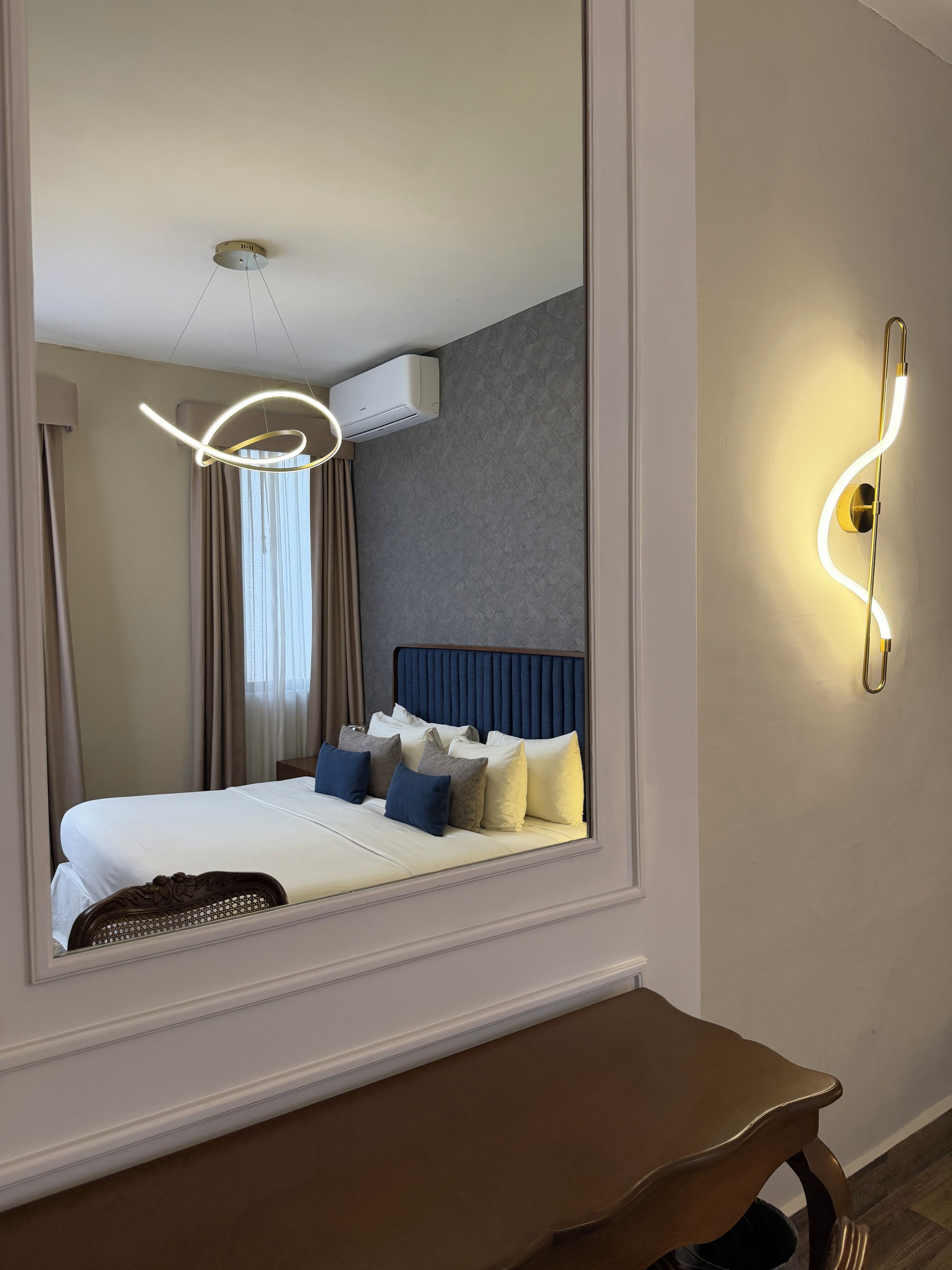 Une chambre d’hôtel avec un grand lit, une table de chevet, un climatiseur fixé au mur et un luminaire fixé au mur.