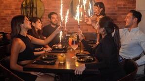 A group of people sitting around a table with sparklers, a brick wall, and a round mirror in the background. - Casa Lucia Hotel Boutique (Mérida)