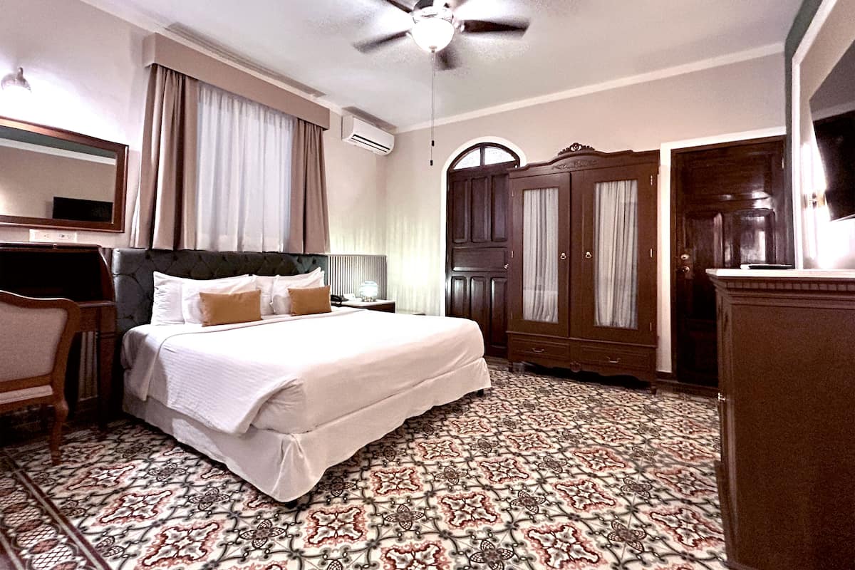 A hotel room with a bed, a desk, a wardrobe, and a ceiling fan.