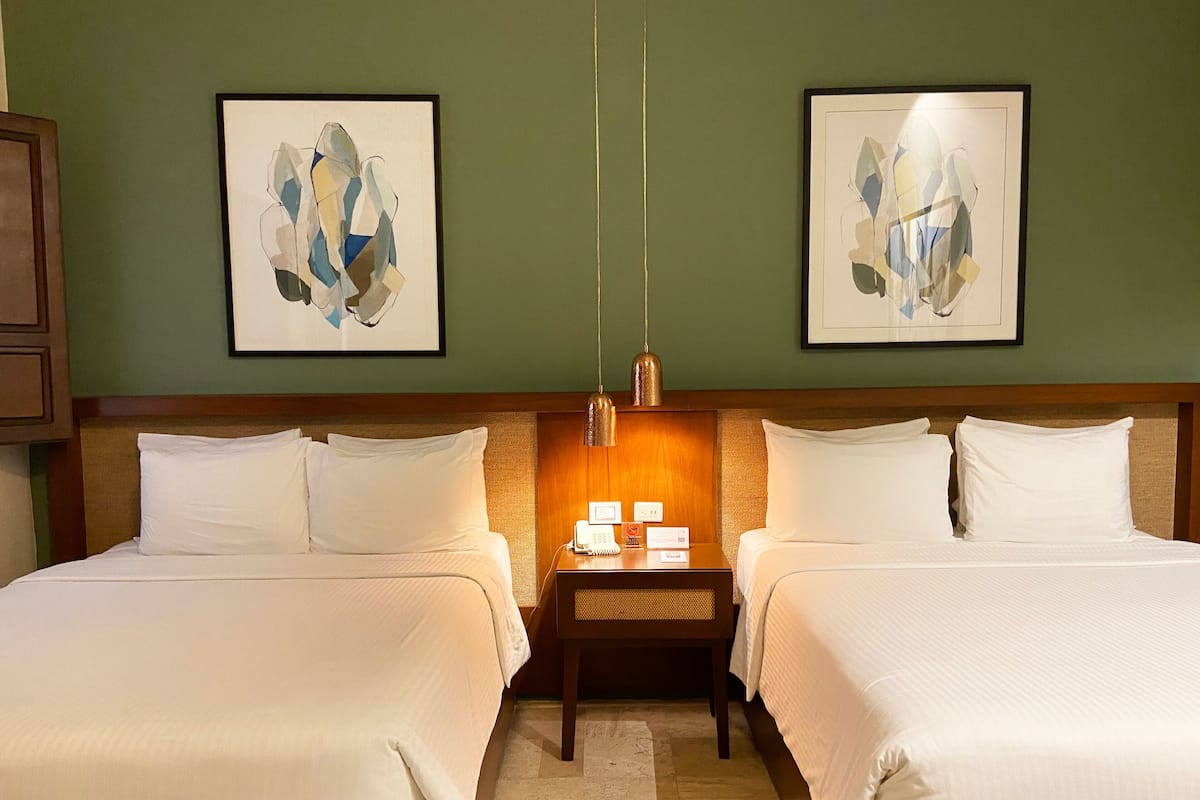 A hotel room with two beds, a nightstand with a phone and a lamp, and abstract art on the walls.