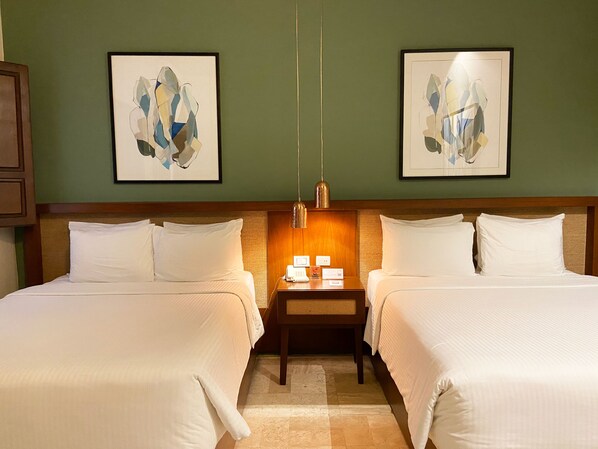 A hotel room with two beds, a nightstand with a phone and a lamp, and abstract art on the walls.