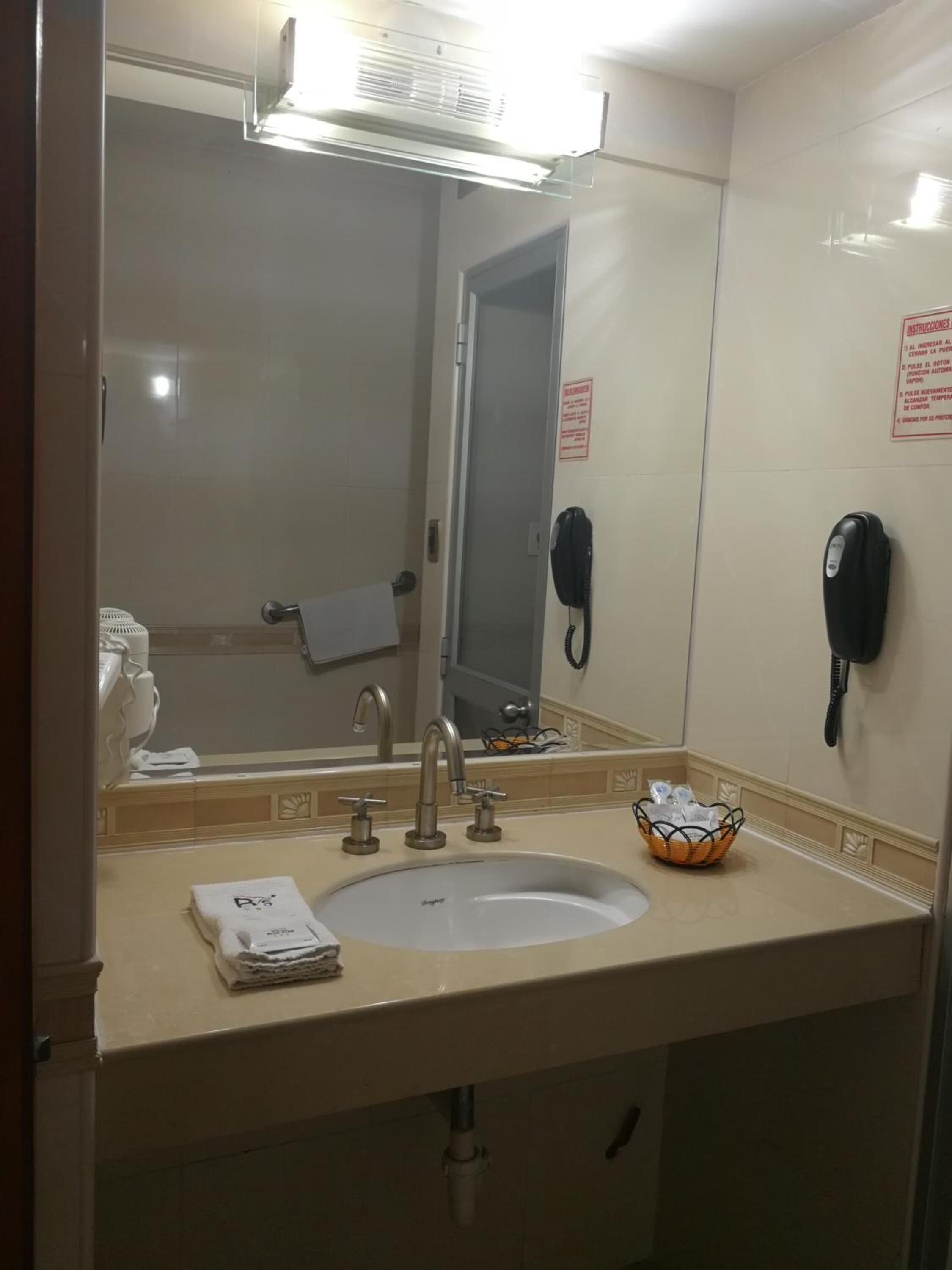 A hotel bathroom with a sink, mirror, towel rack, and a telephone.
