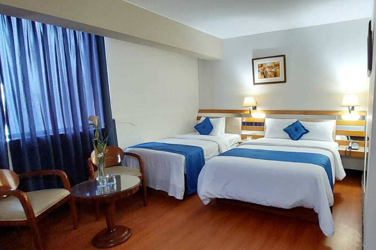 Camera d'albergo con due letti, un tavolino con sedie, una finestra con tende e un telefono fissato al muro.