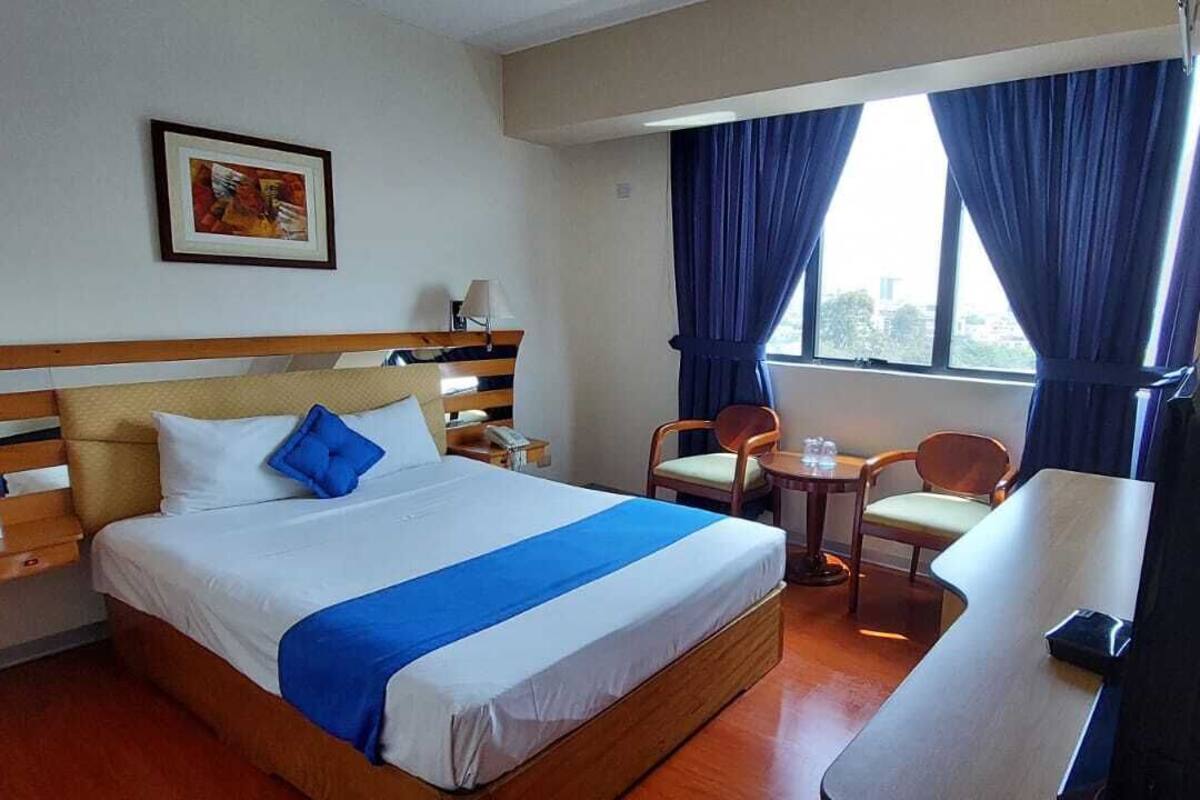 Una camera d'albergo con un letto, una scrivania, una sedia e una finestra con tende.