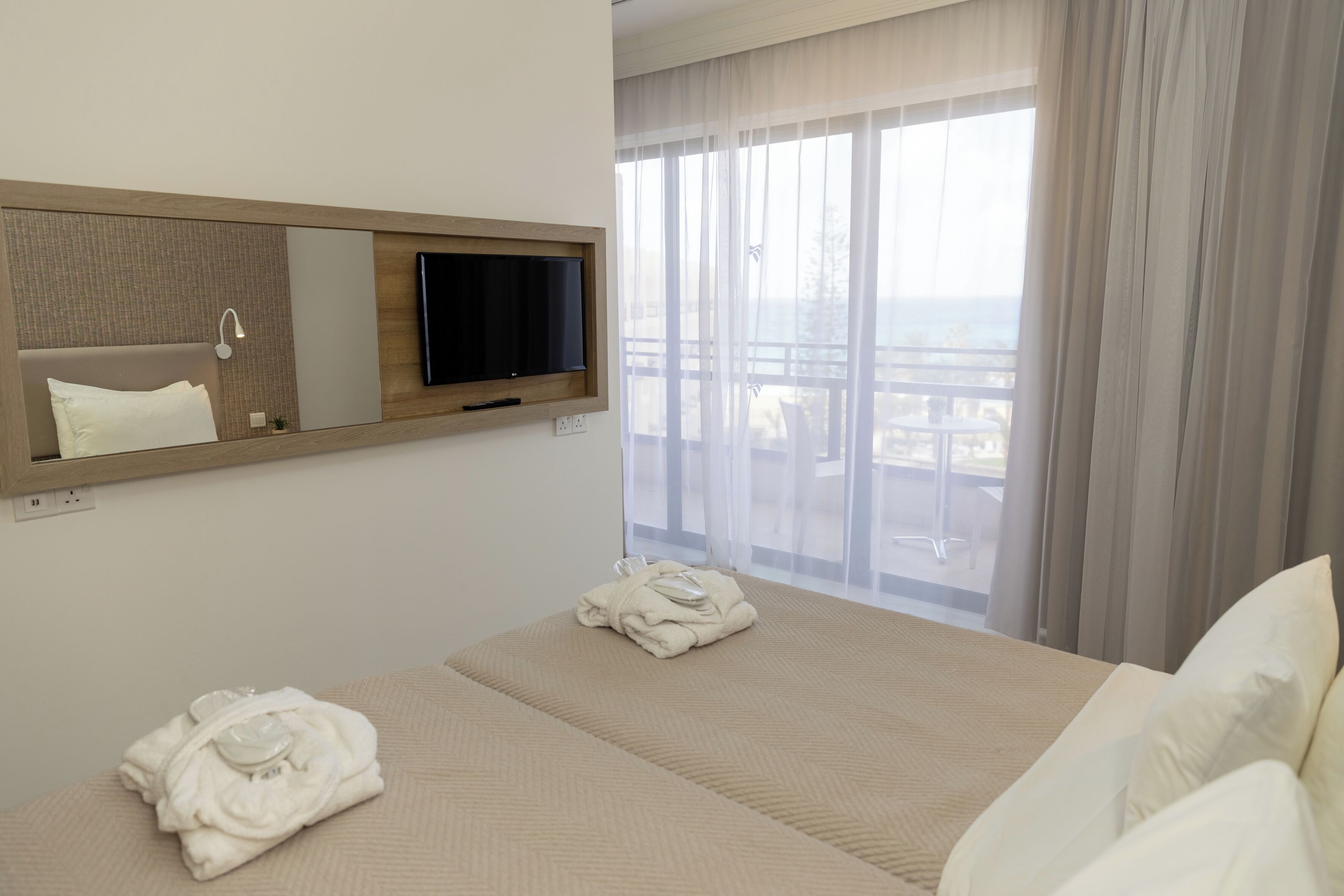 Una habitación de hotel con una cama, televisor, espejo y ventana con cortinas.