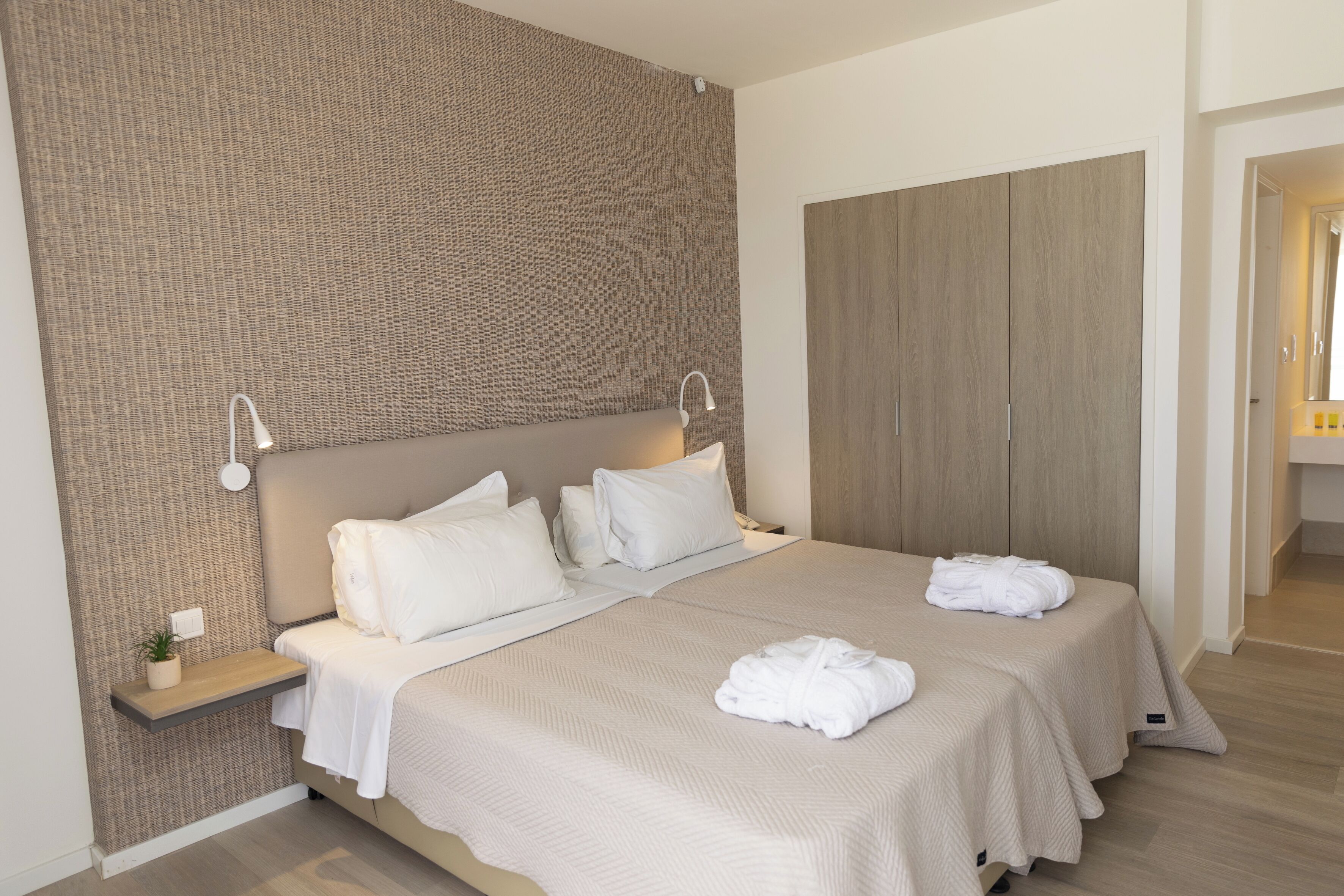 Ett modernt hotellrum med en stor säng, två sängbord, en vägghylla och en garderob i trä.